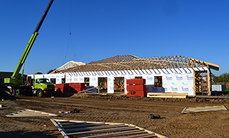 Large building with exposed wall insulation and roof trusses with a crane next to it