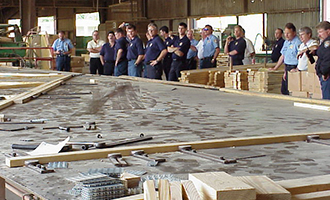 Group of firemen in t-shirts and jeans standing at a large table where trusses are built