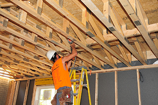 A construction worker on a ladder works on the interior of a second floor truss