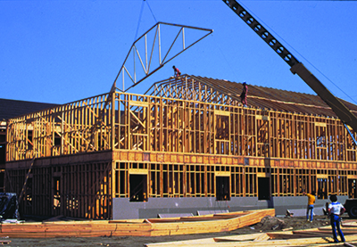 A crane lowers a roof truss into place on top of a second story building