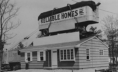 A locomotive train car that reads Reliable Homes Inc sits on top of a single story house