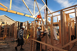 Three construction workers help to attach a roof truss to a building structure