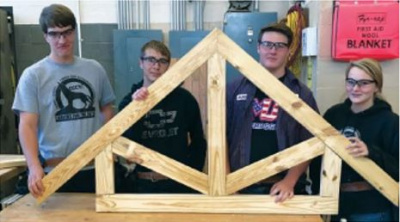 Four students wearing eye protection holding up a small truss