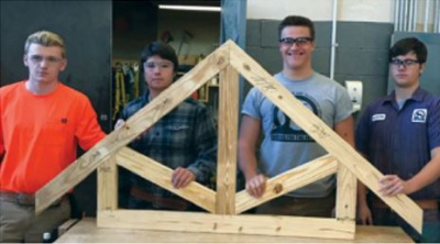 Four students wearing eye protection holding up a small truss