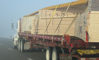 Truck driving on the road is hauling trusses for a delivery